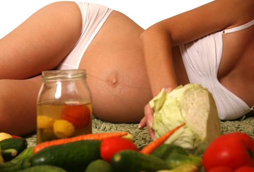 The pregnant woman on a background of various vegetables