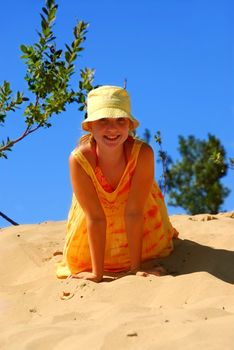 Young girl in yellow hat sitting on top of a sand dune