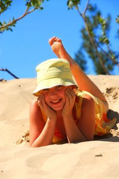 Young girl in yellow hat lying on top of a sand dune