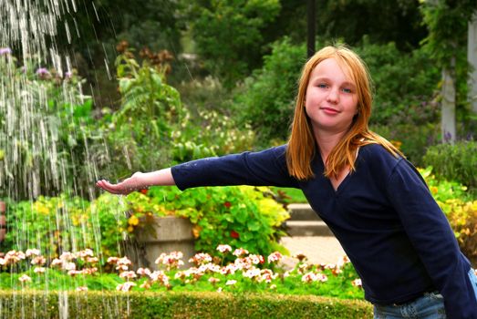 Young girl holding her hand under falling water in a garden