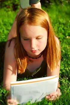 Young girl lying on green grass outside with a notepad