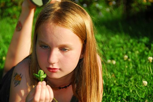 Young girl lying on green grass outside holding a green plant