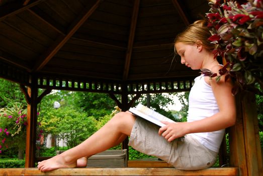 Young girl sitting in a gazeebo reading a book