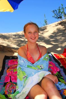 Young girl sitting on a beach wrapped in towels after swimming