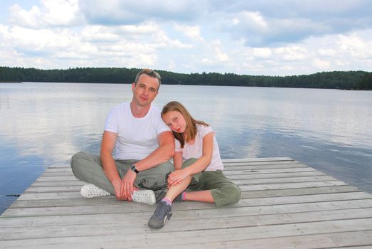 Father and child sitting on a wooden pier on a lake in nothern Ontrario