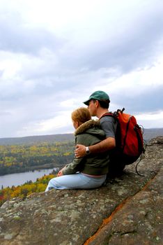 A parent and a child sitting on a cliff edge enjoying scenic view