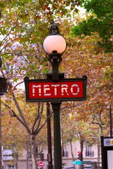 Red metro sign in Paris France on background of fall trees