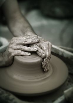 Hands working on pottery wheel , close up retro style toned photo wit shallow DOF