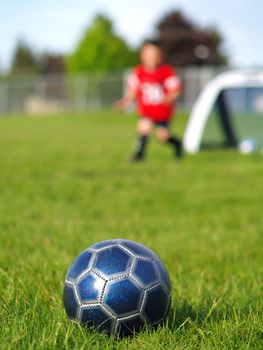 A blue soccer ball on field of green grass on a sunny day with kids in the background.