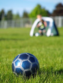 A blue soccer ball on field of green grass on a sunny day with kids in the background.