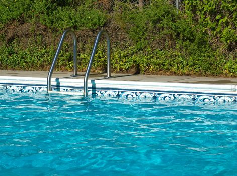 Blue Swimming Pool Water. Ladder, and Pool Edge in Full Sunlight