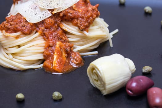 Spaghetti bolognaise in black plate with olives