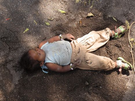 A poor homeless child sleeping on the soil outside a construction site in India.                               