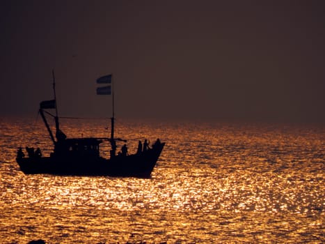 A fishing boat crusing on the golden sea waters.