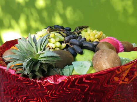 A basket full of fresh fruits like grapes, pineapple, pear, chickoo and others.                               