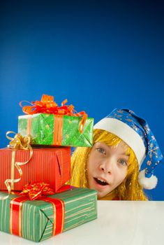 Surprised teen girl looking from behind the Christmas presents