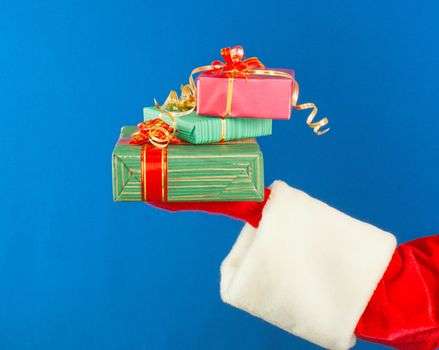 Santa's hand holding presents over blue background