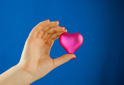 Hand holds a heart shaped gift against blue background