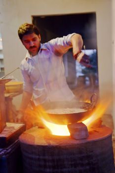 Kashmir Jammu, Northern India, Himalayas - December 18, 2011; Vertical portrait of Roadside cafe chef stirring the pot of curry in a wok over a tandoor hob in Jammu Kashmir Himalayan region of Northern India with crop margings