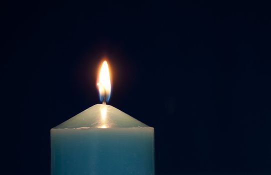 Close up of burning candle against dark blue background