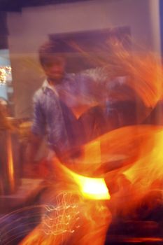 Vertical portrait and motion blur of a cook at Northern Indian roadside eatery flash frying on a tandoor tandoori oven with sparks flying from an open wok and flame from the cooking source, crop margins and copy areas