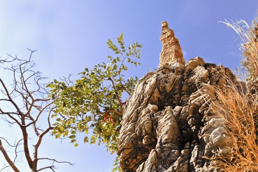 Horizontal landscape of rock formation and man made rock structure, some made made with trees framing a Hindu spritual ribbon tied high up a cliff on a bush. The path is a holy pilgrimage for Hiduism, crop margins and negative spaces