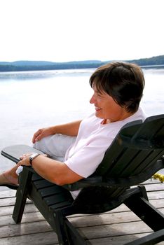 Mature woman relaxing on a pier in a wooden chair