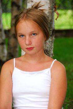Portrait of a young pretty girl sitting under a birch tree in a park