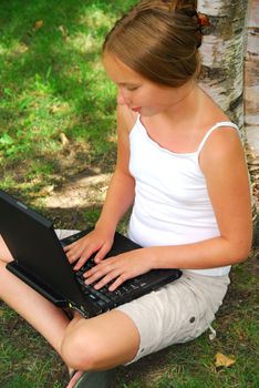 Young girl sitting in a park with laptop computer