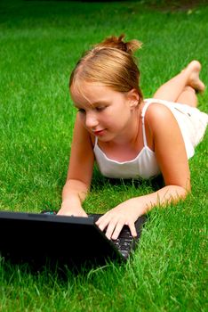 Young girl lying on grass in a park with laptop computer