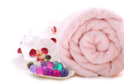 Pink rolled up towel with bath beads on white background