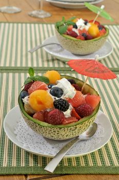Summer fruit salads served in melon and topped with whipped cream and mint leaves