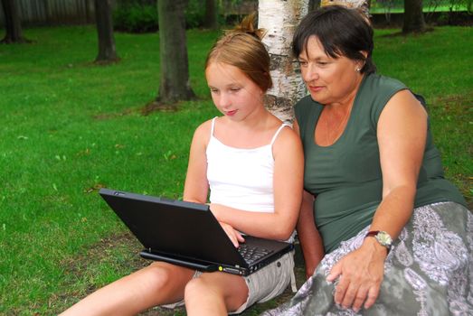 Grandmother and granddaughter sitting outside with laptop computer