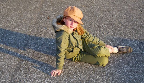 Girl in fall clothes sitting on asphalt pavement