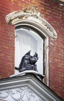 Gargoyle perched in front of a window on a dilapidated brick house.