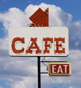 Old cafe sign with the word "eat" against a cloudy sky.