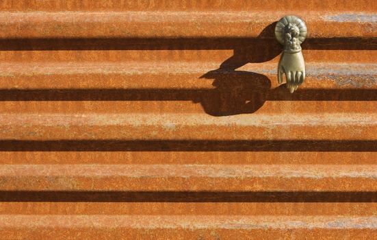 Brass hand of Buddha hanging on a rusted corrugated metal wall.