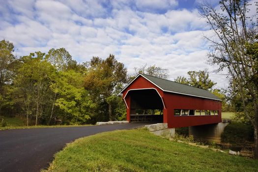 Red covered bridge over a stream during Fall.