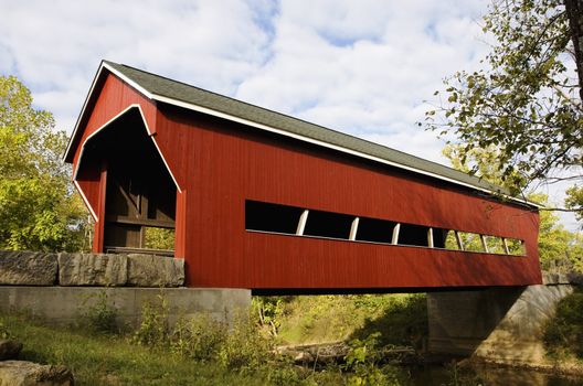 Red covered bridge over a stream during Fall.