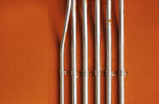 Shiny metal utility pipes mounted on a bright orange painted plaster wall.