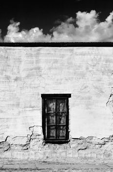 Window with curtains on a boarded and abandoned adobe building.