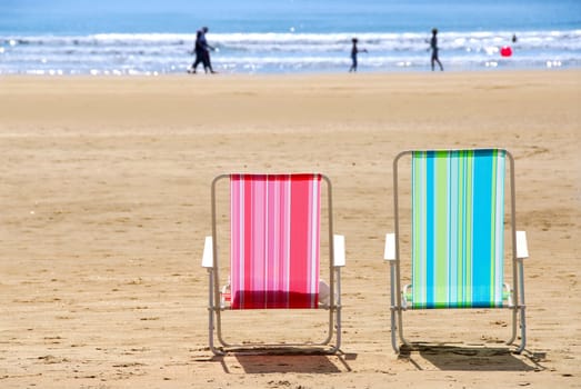 Two empty colorful beach chairs on a sandy beach