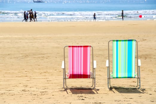 Two empty colorful beach chairs on a sandy beach