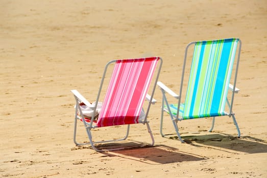 Two empty colorful beach chairs on a sandy beach