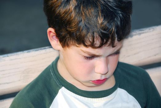 Portrait of a sad boy sitting on a bench in a park