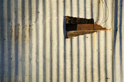 Rusty corrugated metal with a late-day shadow and a ragged hole.