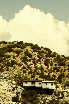 Miner's shack on a steep hill with a cloud in the background.