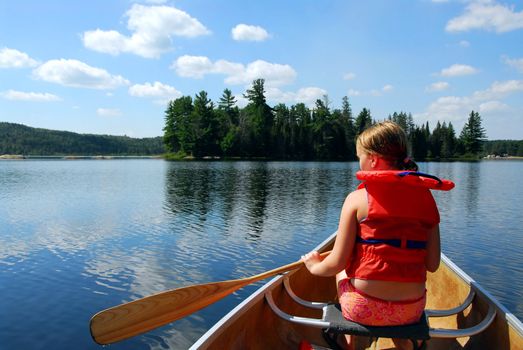 Young girl in canoe paddling on a scenic lake