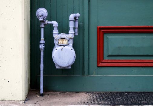 Blue gas meter against a green exterior wall with red trim.