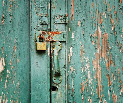 Rusty, unused lock on an old wooden door with peeling paint.